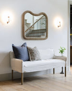 White sofa with decorative pillows under a heart-shaped mirror in a well-lit room.