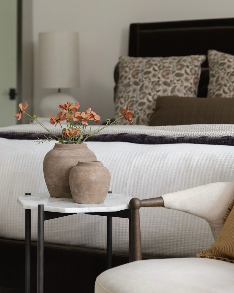 Decorative setting with a small table holding vases and flowers in a bedroom.