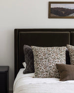 Bed with patterned and solid pillows against a neutral wall with a framed picture.