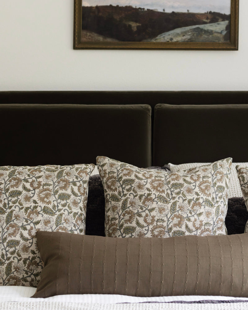 Bed with patterned pillows and a framed landscape painting above the headboard.