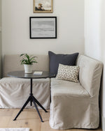 Beige sofa with cushions and a small round table in a room with framed artwork on the wall.