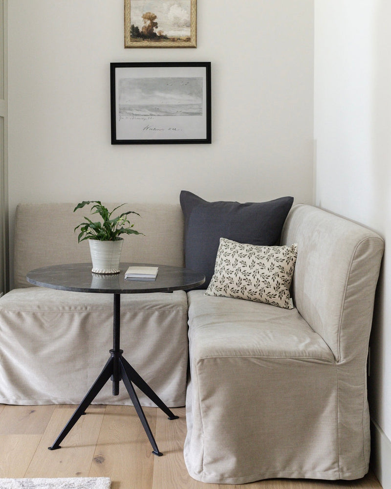 Beige sofa with cushions and a small round table in a room with framed artwork on the wall.