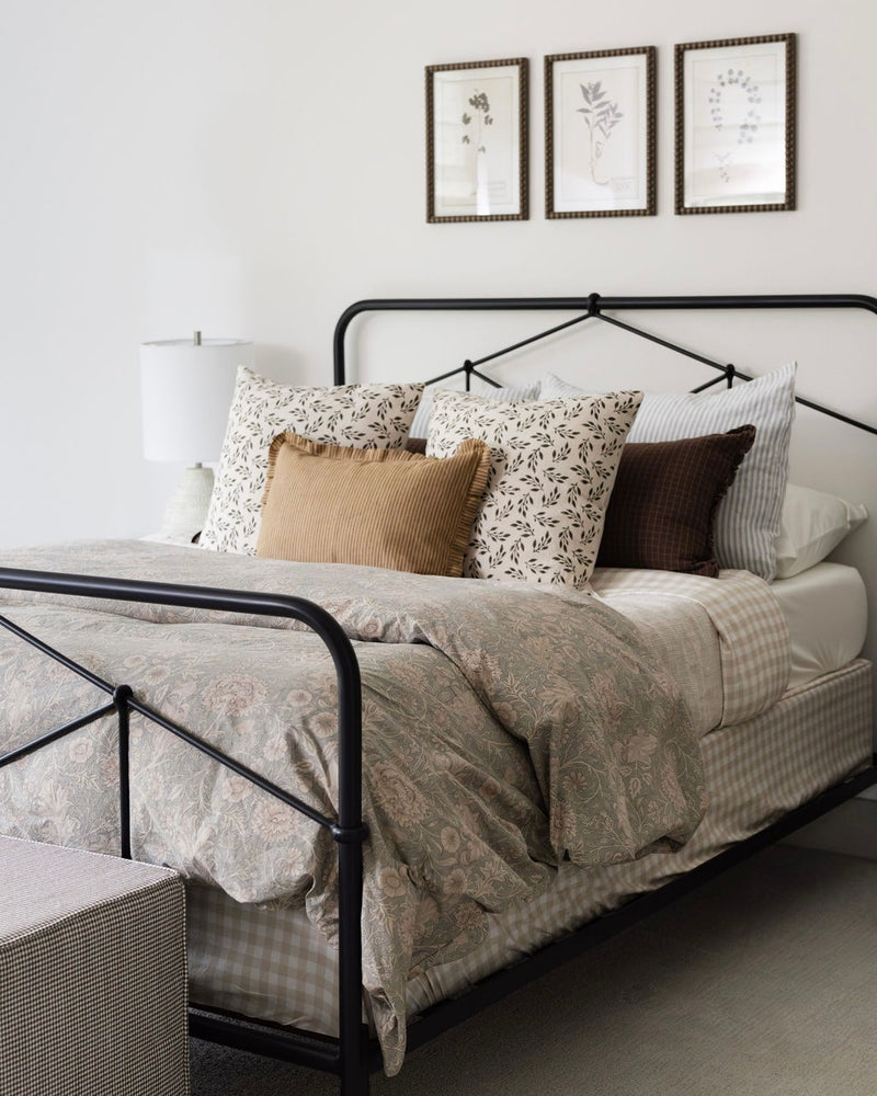 Bedroom with a bed featuring patterned pillows and a black metal frame, with three framed pictures on the wall.