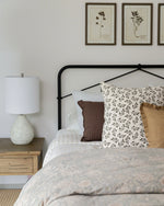 Bedroom with a bed featuring patterned pillows, a lamp on a nightstand, and framed artwork on the wall.