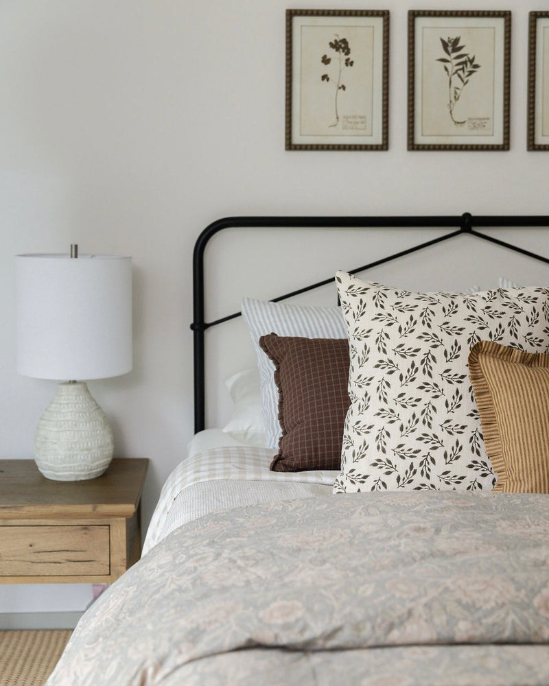Bedroom with a bed featuring patterned pillows, a lamp on a nightstand, and framed artwork on the wall.