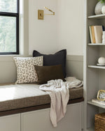Window seat with pillows and a blanket in a cozy room with shelves and a wall sconce.