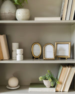 Decorative bookshelf with books, vases, and picture frames against a neutral wall.
