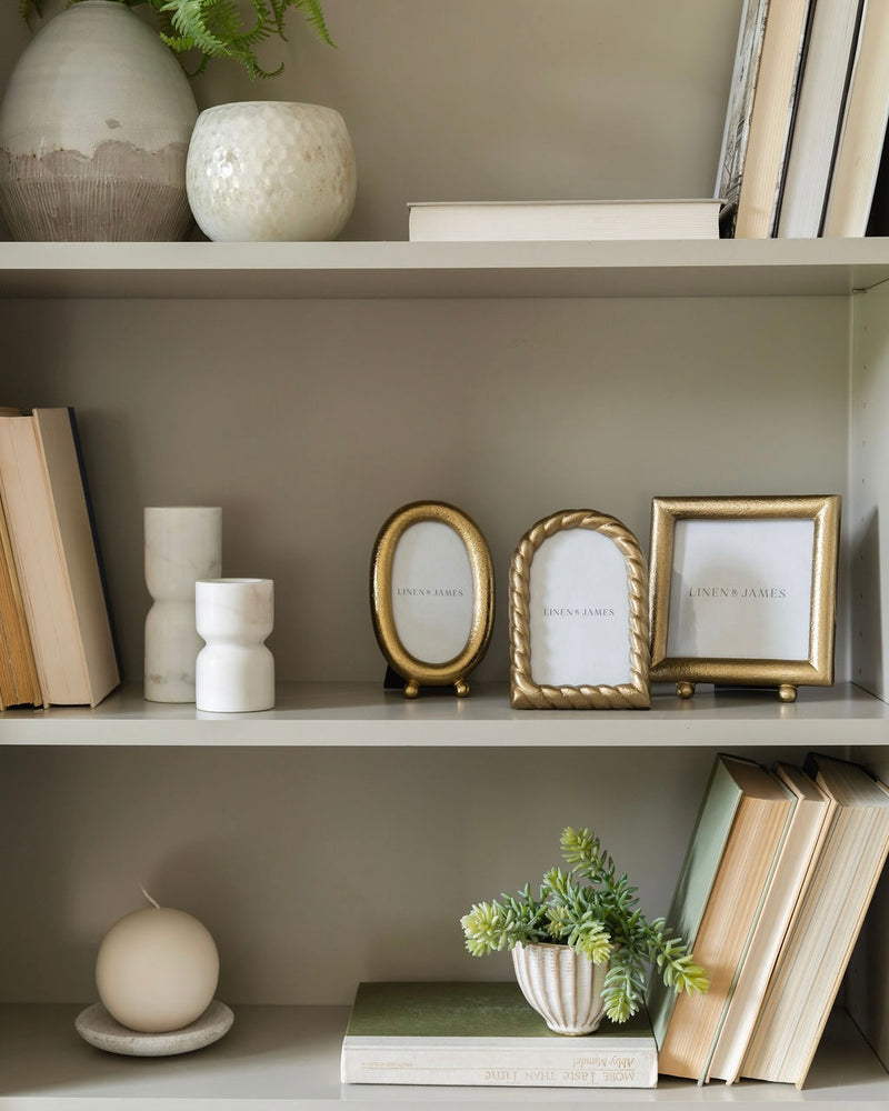 Decorative bookshelf with books, vases, and picture frames against a neutral wall.