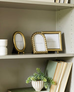 Gold picture frames on a shelf with books and a plant