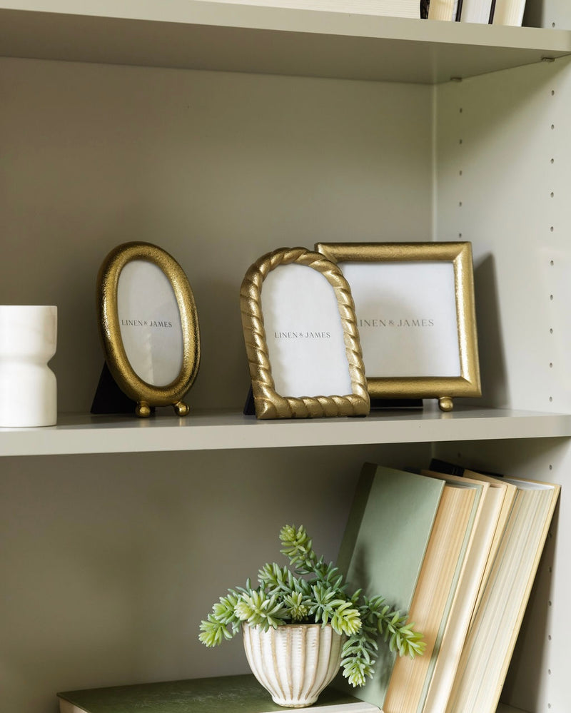 Gold picture frames on a shelf with books and a plant