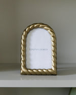 Gold rope-style picture frame on a white surface with a neutral background