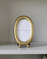 Gold oval photo frame on a white surface with a blurred background