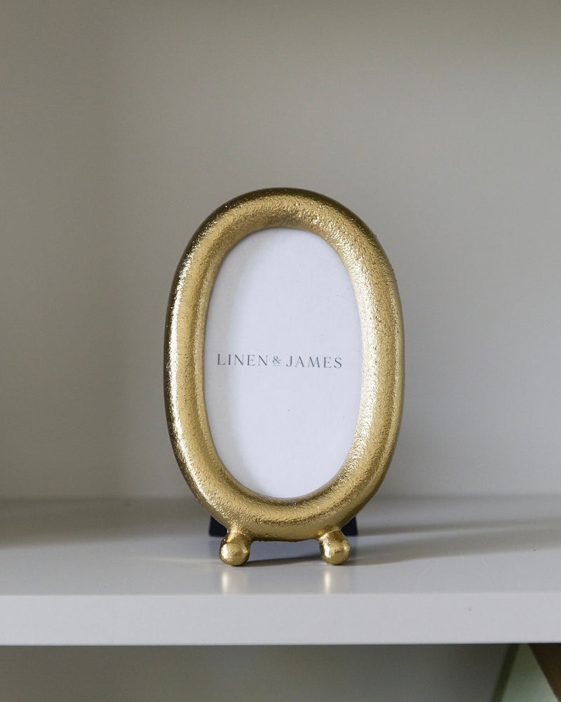 Gold oval photo frame on a white surface with a blurred background
