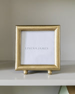 Gold picture frame with 'Linen & James' branding on a white surface.